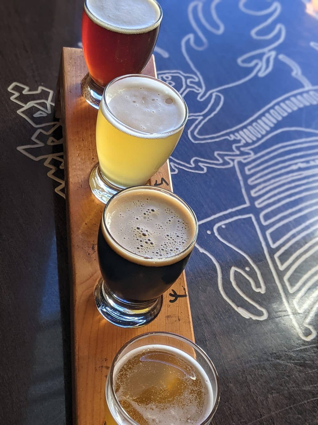 A flight of New Level beers, red, golden, dark and amber, on a wooden paddle over their blue table art